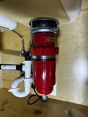 Red garbage disposal installed beneath a kitchen sink, shared by Mulhearn Plumbing on Yelp